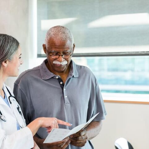 The senior adult man looks at the brochure in his hands as the mid adult female doctor explains the options detailed there.